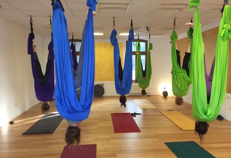 Yoga-Übenden hängen kopfüber in Aerial-Yoga Tüchern in der Position der "Fledermaus"